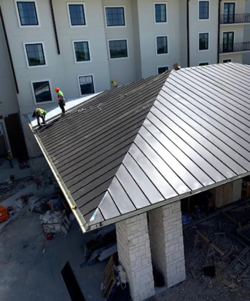 Crew installing standing seam metal roof panels on a commercial project in Sinton